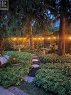 Landscaped garden featuring mature trees, string lighting, a stone pathway, and lush ground cover - 