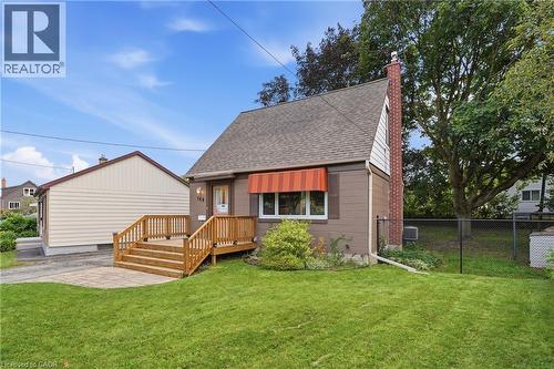 Front exterior with a wood deck entrance, red striped awning, asphalt shingle roof, and a brick chimney - 160 Lorne Crescent, Kitchener, ON 