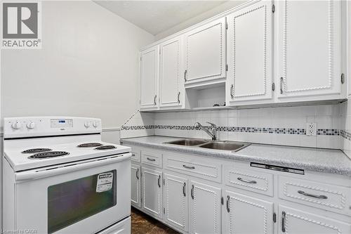 Kitchen featuring white upper and lower cabinetry, a built-in double basin sink, and a white electric range - 160 Lorne Crescent, Kitchener, ON 