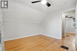 Sloped ceiling room featuring wood-finish flooring, ceiling fan with integrated lighting, and a white paneled door - 