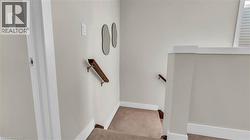Carpeted staircase featuring a wood handrail and light-toned wall paint - 