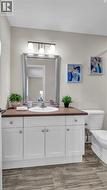 White vanity with panel doors and drawers, a built-in sink, a dark countertop, and a framed mirror - 