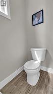 White toilet with wood-finish tile flooring and light-colored walls - 