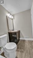 Bathroom with wood-finish tile flooring, a dark wood-finish vanity with a white countertop, and a rectangular framed mirror - 