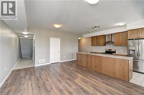 Open-concept living area with wood-finish flooring, kitchen island, and stainless steel appliances - 102 Wheat Lane, Kitchener, ON 