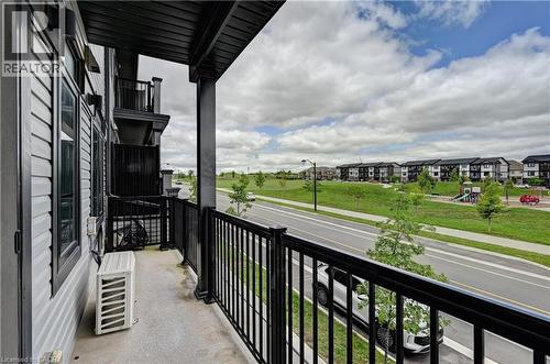 Spacious second-floor balcony with black metal railings and concrete decking, overlooking manicured green space and new residential community - 102 Wheat Lane, Kitchener, ON 