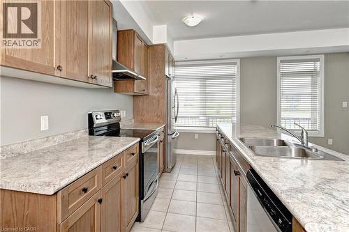 Galley kitchen featuring wood cabinetry, light-toned countertops, and stainless steel appliances - 102 Wheat Lane, Kitchener, ON 