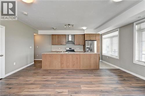 Open-concept kitchen and dining area featuring wood-finish cabinetry, stainless steel appliances, a center island with seating, and wood-finish plank flooring throughout - 102 Wheat Lane, Kitchener, ON 