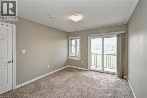 Neutral-toned walls, plush carpet flooring, a white paneled door, sliding glass doors leading to a balcony, and a window with blinds - 102 Wheat Lane, Kitchener, ON 