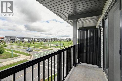 Spacious covered balcony with black metal railing and composite decking, overlooking manicured community grounds with mature landscaping and planned streetscape - 102 Wheat Lane, Kitchener, ON 