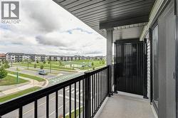 Spacious covered balcony with black metal railing and composite decking, overlooking manicured community grounds with mature landscaping and planned streetscape - 