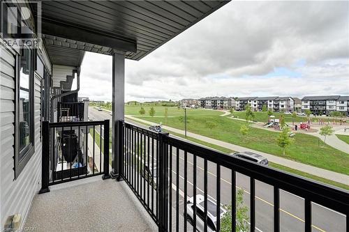 Spacious covered balcony with black aluminum railing overlooking expansive green space and new residential development - 102 Wheat Lane, Kitchener, ON 
