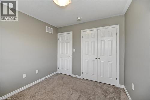 Neutral-toned walls with carpet flooring, featuring a paneled door and bi-fold closet doors - 102 Wheat Lane, Kitchener, ON 