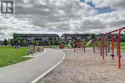 Community park featuring a playground area with swings and a slide structure, surrounded by green spaces and a paved walking path - 102 Wheat Lane, Kitchener, ON 