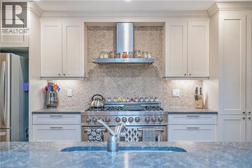 Chef's kitchen featuring custom cabinetry, professional-grade range with multiple burners, integrated range hood, mosaic tile backsplash, and stainless steel appliances. - 115 Southwood Drive, Cambridge, ON 