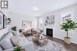Living area featuring a fireplace with a white mantle, dark wood-finish flooring, white walls, multiple windows with white plantation shutters, and a semi-flush ceiling light fixture - 
