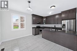 Kitchen featuring dark wood-finish cabinetry, stainless steel appliances, and a central island with a sink and dark countertop - 