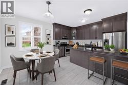 Open-concept kitchen and dining area featuring dark wood-finish cabinetry, stainless steel appliances, a center island with countertop seating, and light-toned tile flooring - 