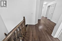 Hallway featuring wood-finish flooring, white baseboards, and white paneled doors with dark hardware - 