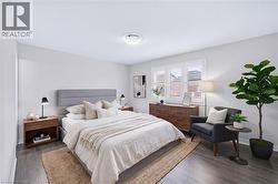 Contemporary bedroom featuring wood-finish flooring, a window with plantation shutters, a light gray upholstered headboard, and recessed ceiling lighting - 