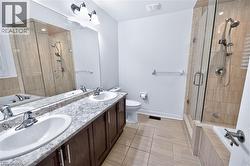Bathroom featuring a dual vanity with undermount sinks and a patterned countertop, a glass-enclosed shower with tiled walls, a separate built-in tub, and light-toned tile flooring - 