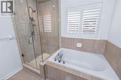 Bathroom featuring a corner soaking tub, a glass-enclosed shower with a handheld showerhead, and a window with plantation shutters - 