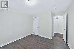 Room featuring light-toned walls, wood-finish flooring, white baseboards, and a paneled interior door with dark hardware - 