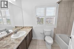 Bathroom featuring a white bathtub with tiled surround, a toilet, and a vanity with a single basin sink - 