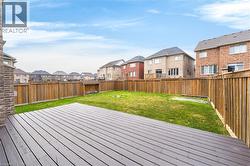 Expansive backyard featuring a large wood-finish deck, vibrant green lawn, and full perimeter wood fencing - 