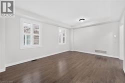 Spacious room featuring wood-finish flooring, white plantation shutters, and a tray ceiling - 
