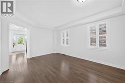 Spacious room featuring wood-finish flooring, white plantation shutters on two windows, and tray ceiling detail - 