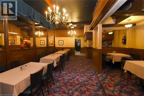 Elegant private dining room featuring warm wood-paneled walls, ornate crystal chandelier, recessed ceiling lighting, and patterned carpet flooring - 942-946 Barton Street E, Hamilton, ON 