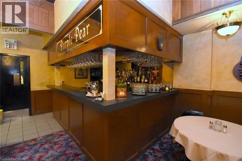 Distinctive corner bar featuring rich wood cabinetry, mirrored back panel with bottle display, and a dark countertop - 942-946 Barton Street E, Hamilton, ON 