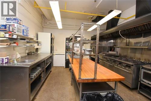Professional Commercial Kitchen featuring stainless steel prep counters, dual commercial-grade ovens, overhead exhaust hood system, open shelving with metal framework, fluorescent ceiling lighting, an - 942-946 Barton Street E, Hamilton, ON 