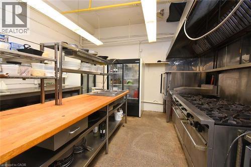 Professional commercial kitchen featuring stainless steel six-burner range with overhead ventilation hood, wood-finish prep counter with understorage shelving, commercial-grade refrigeration unit, and - 942-946 Barton Street E, Hamilton, ON 