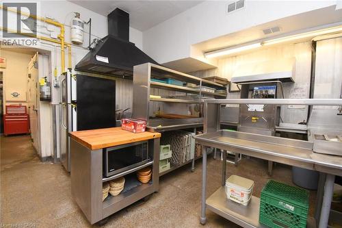 Professional commercial kitchen featuring stainless steel prep tables and shelving, black ventilation hood with canopy, wood-finish countertop work surface, and integrated storage throughout - 942-946 Barton Street E, Hamilton, ON 