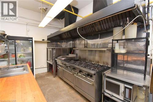 Professional-grade commercial kitchen featuring a six-burner range with double ovens, stainless steel backsplash and countertops, overhead exhaust hood system, and integrated refrigeration units - 942-946 Barton Street E, Hamilton, ON 