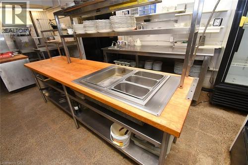 Professional-grade commercial kitchen featuring stainless steel prep tables with integrated sink stations, overhead storage shelving with organized workspace, and commercial-grade appliances including - 942-946 Barton Street E, Hamilton, ON 