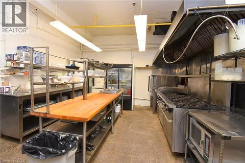 Professional kitchen featuring stainless steel cooking equipment, including a six-burner range and ventilation hood, alongside a wood-finish prep table with storage below - 942-946 Barton Street E, Hamilton, ON 