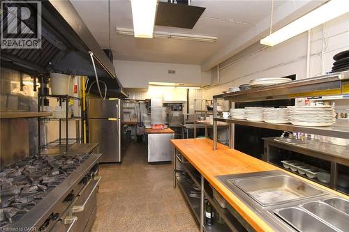 Professional commercial kitchen featuring stainless steel countertops, multiple cooking stations with gas ranges, commercial-grade refrigeration, overhead ventilation system, open shelving for plate a - 942-946 Barton Street E, Hamilton, ON 