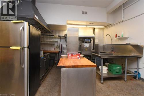 Professional kitchen featuring stainless steel appliances, including refrigerator, range, and ice maker; wood-finish island with prep space; stainless steel work tables and shelving; commercial-grade - 942-946 Barton Street E, Hamilton, ON 