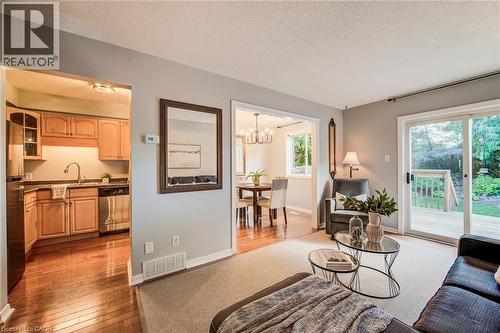 Hardwood flooring in the kitchen, light wood cabinetry, stainless steel dishwasher, glass sliding doors to the exterior deck, and an overhead dining room chandelier - 360 Cornridge Place Unit# 2, Waterloo, ON 