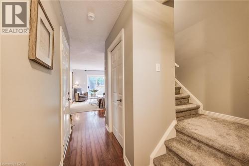 Hallway with wood-finish flooring, white doors, and a carpeted staircase - 360 Cornridge Place Unit# 2, Waterloo, ON 