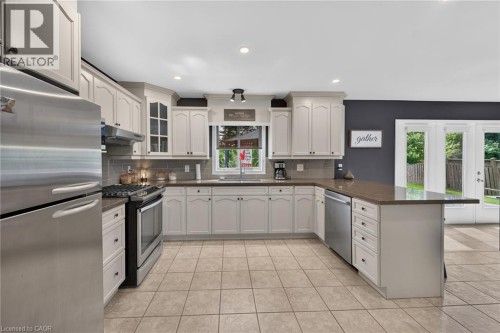 U-shaped kitchen featuring light-toned cabinetry, stainless steel appliances, a tile backsplash, and a breakfast bar - 10 Balvenie Boulevard, Caledonia, ON 