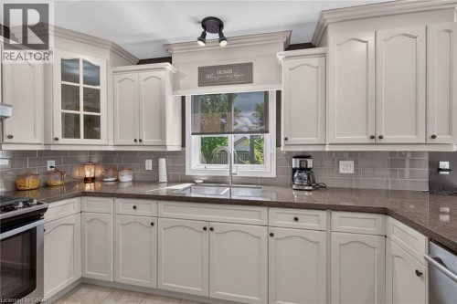 White cabinetry with crown molding, dark countertops, tiled backsplash, built-in sink, and stainless steel appliances - 10 Balvenie Boulevard, Caledonia, ON 