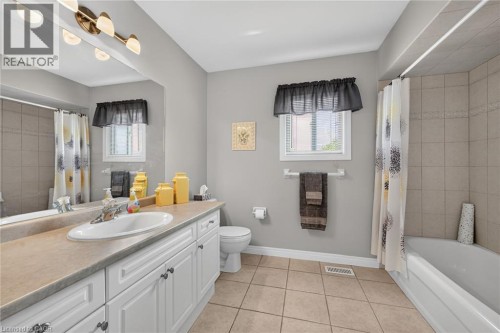 Full vanity mirror, white cabinetry, integrated sink, tiled flooring, and a shower-tub combination with tiled surround - 10 Balvenie Boulevard, Caledonia, ON 