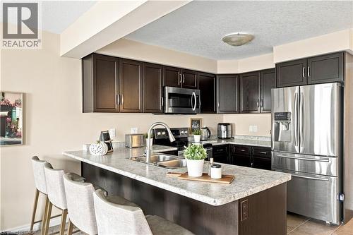 Dark wood-finish cabinetry, stainless steel appliances, speckled countertops, kitchen island with integrated sink, and recessed ceiling lighting - 187 Eden Oak Trail, Kitchener, ON 