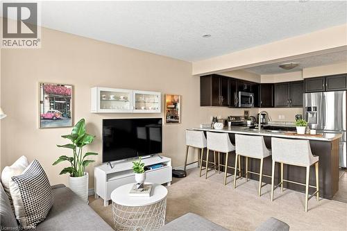Open-concept living space featuring dark wood-finish cabinetry, stainless steel appliances, a kitchen island with seating, and light-toned walls - 187 Eden Oak Trail, Kitchener, ON 