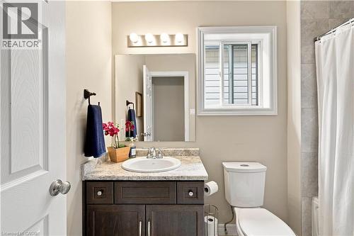 White paneled door, dark wood-finish vanity with an integrated sink, stone-look countertop, rectangular mirror, and a white framed window - 187 Eden Oak Trail, Kitchener, ON 