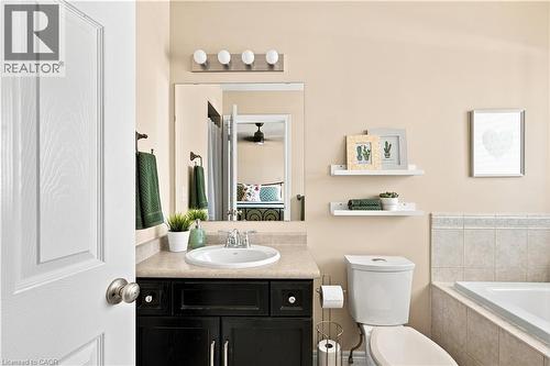 Bathroom featuring a dark wood-finish vanity with an integrated sink and light-toned countertop, a wall-mounted mirror, and a built-in bathtub with tiled surround - 187 Eden Oak Trail, Kitchener, ON 